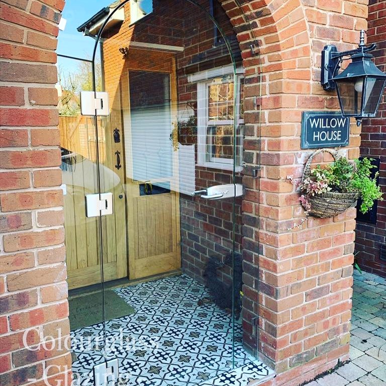 Bespoke frameless glass door installed in a brick archway entrance at a residential property.